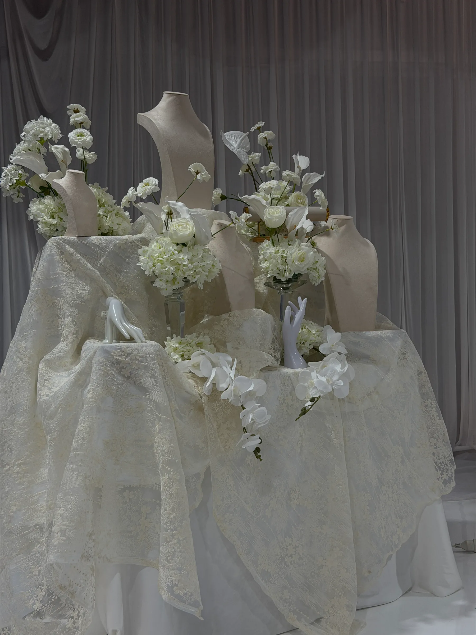 Tables styling by Decoration X: Lace-draped display table of velvet jewellery busts and mannequin hands among white roses, hydrangeas, calla lilies and orchids.