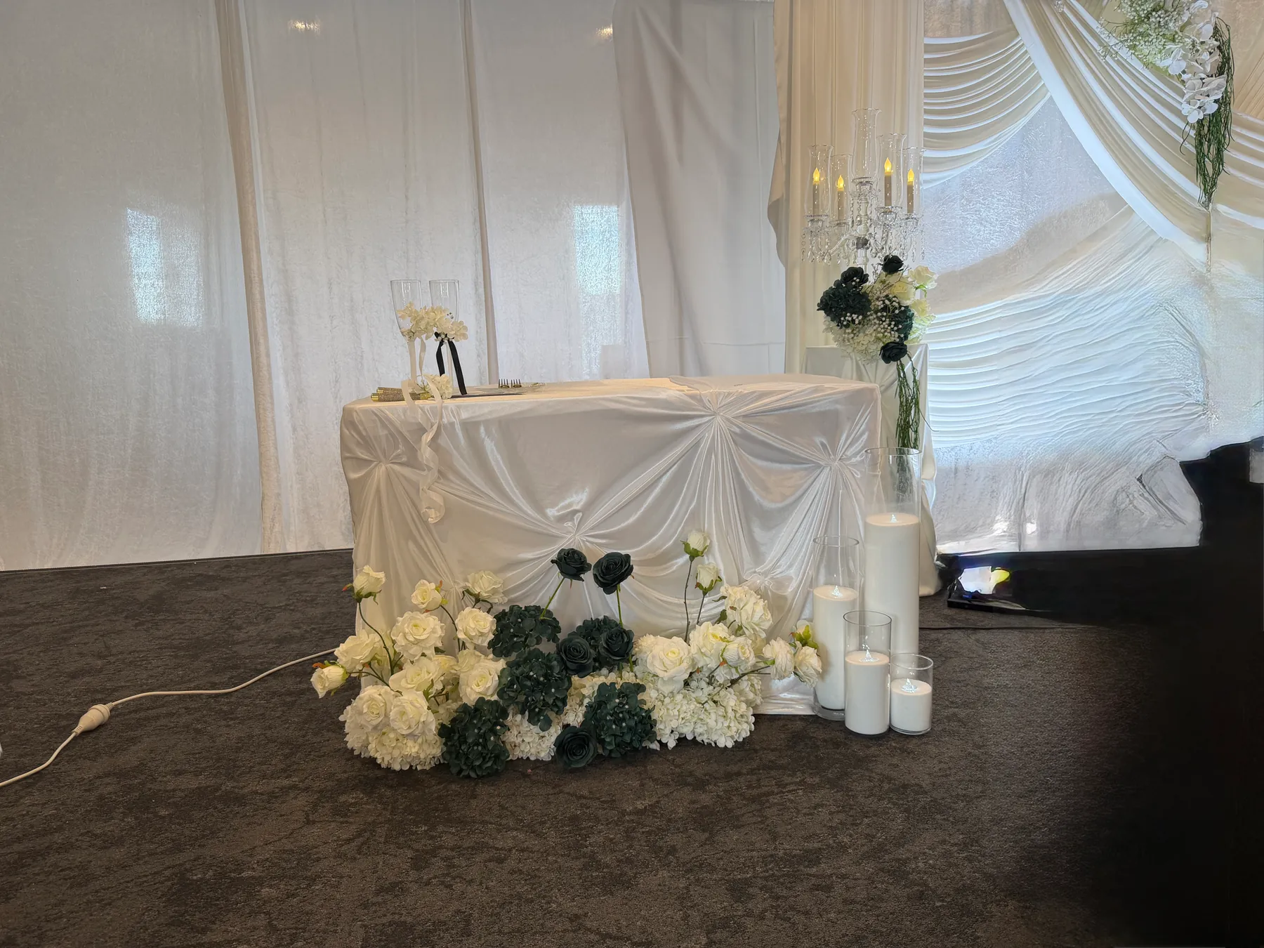 Ceremony styling by Decoration X: Signing table in gathered ivory satin with champagne flutes, white roses, dark green roses and hydrangea at its base and pillar candles in glass.