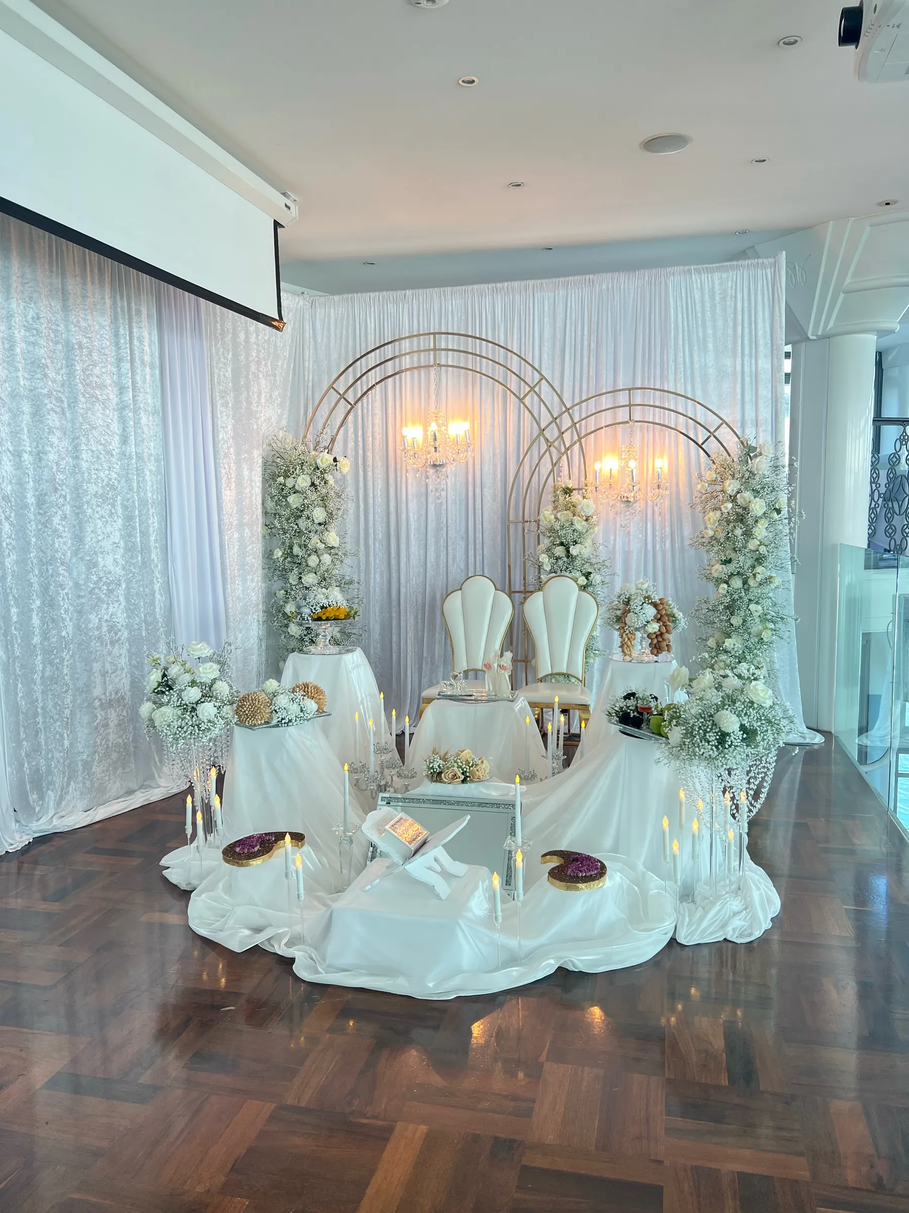 Cultural styling by Decoration X: Sofreh aghd in white satin with candles, a Quran stand and mirror, two white shell chairs under gold double arches with gypsophila and crystal chandeliers.