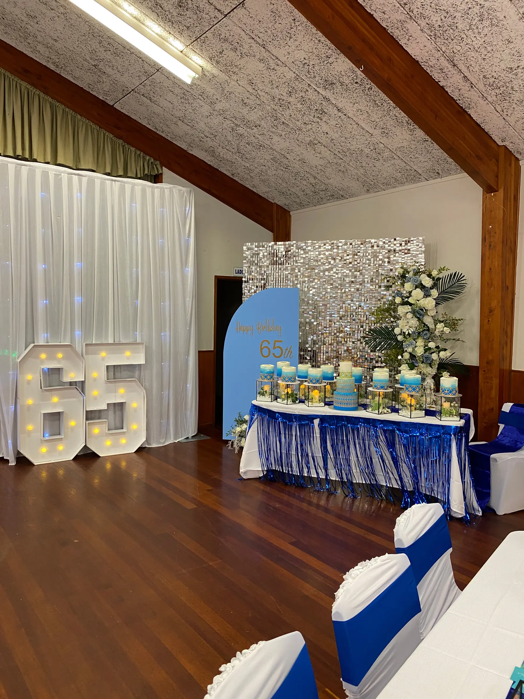 Birthday styling by Decoration X: '65' marquee numbers, gold sequin wall, blue tablescape.