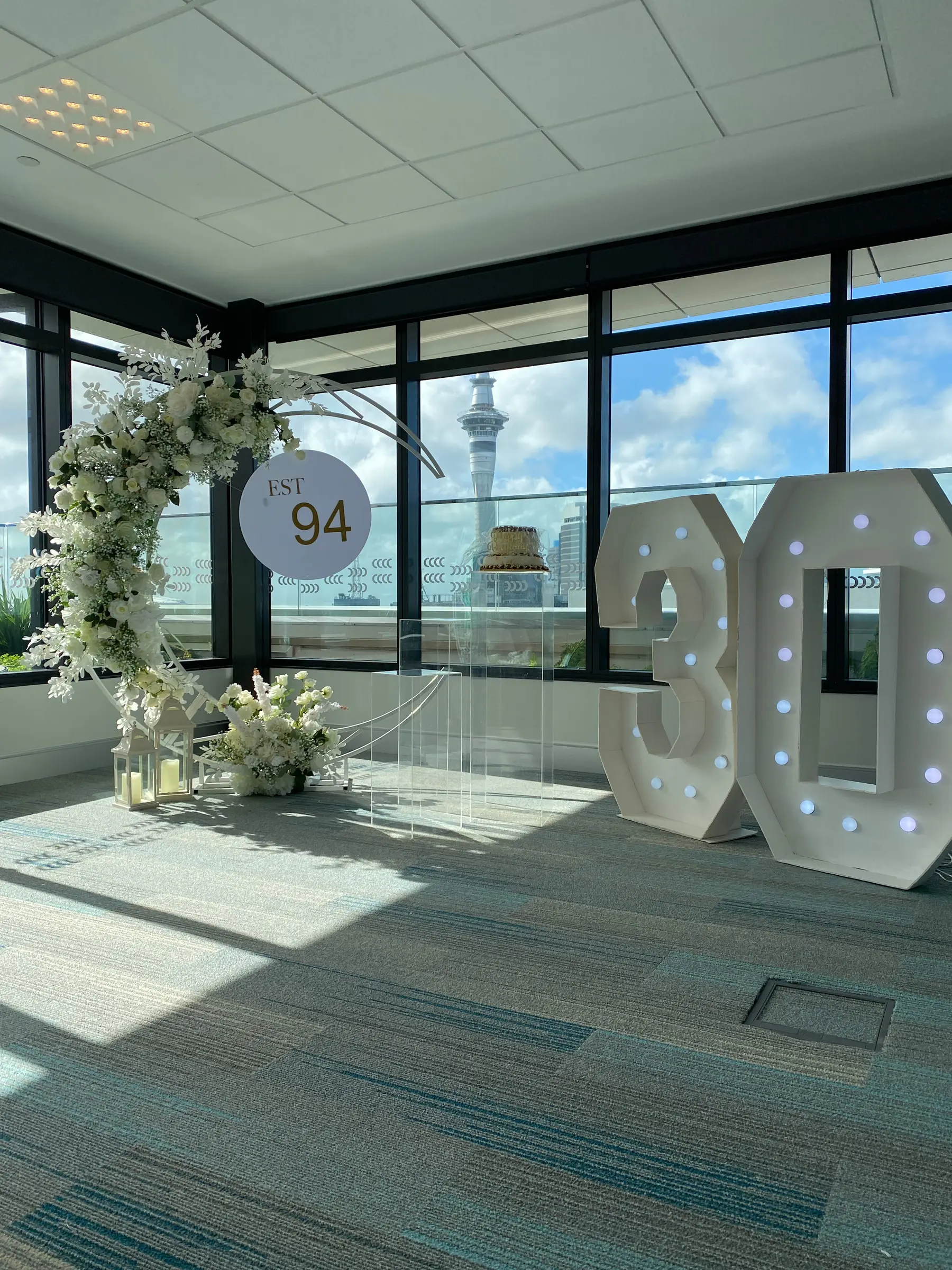 Birthday styling by Decoration X: '30' marquee numbers, 'EST 94' sign, Sky Tower through window; office carpet.