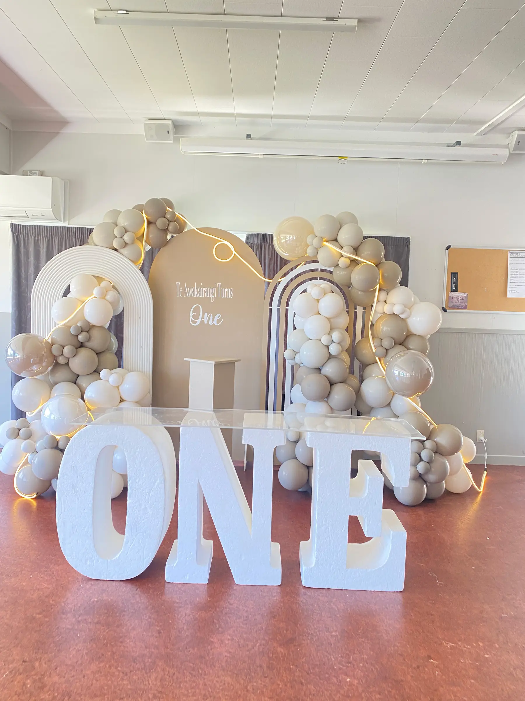 Birthday styling by Decoration X: 'ONE' marquee letters, neutral balloons; 'Te Awakairangi turns one'.