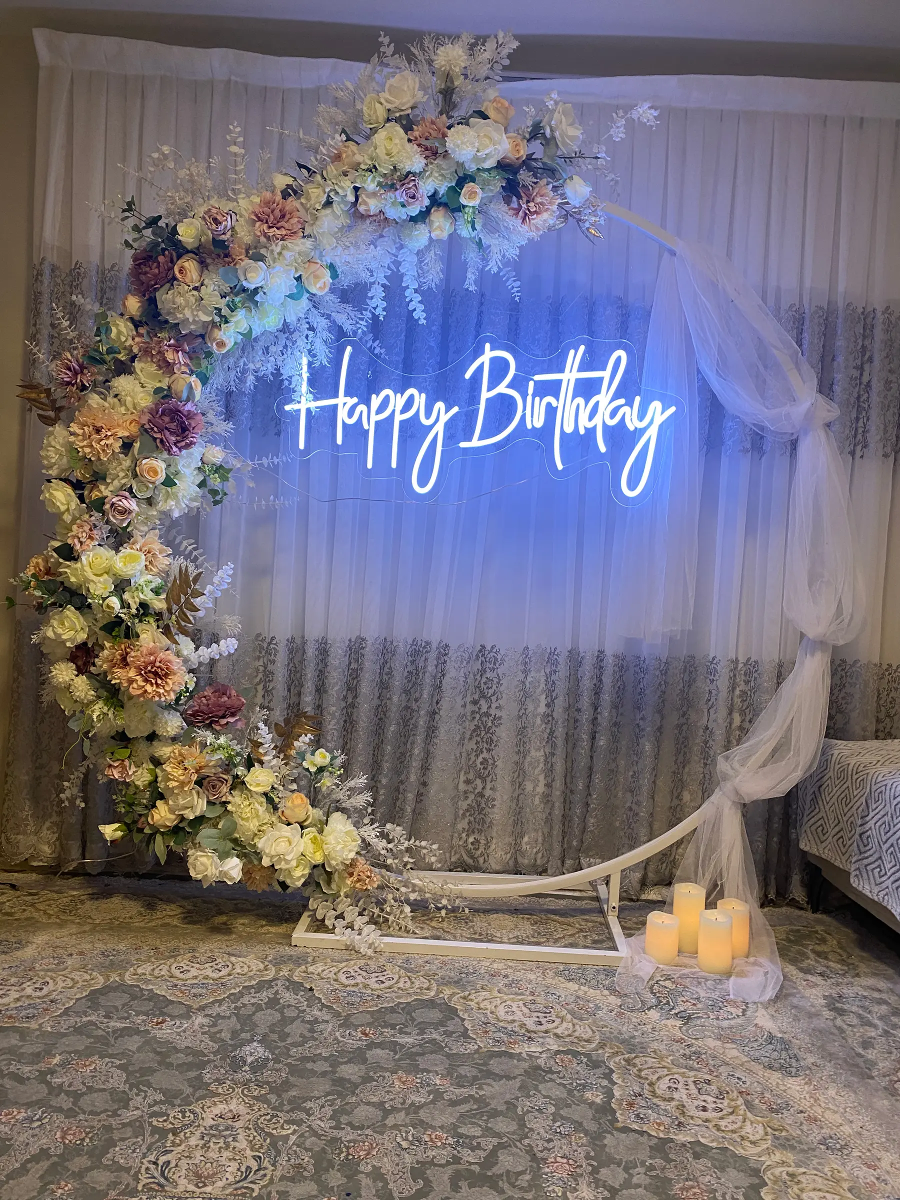 Signage styling by Decoration X: 'Happy Birthday' blue neon on floral moon arch, tulle, candles; bed edge at right.