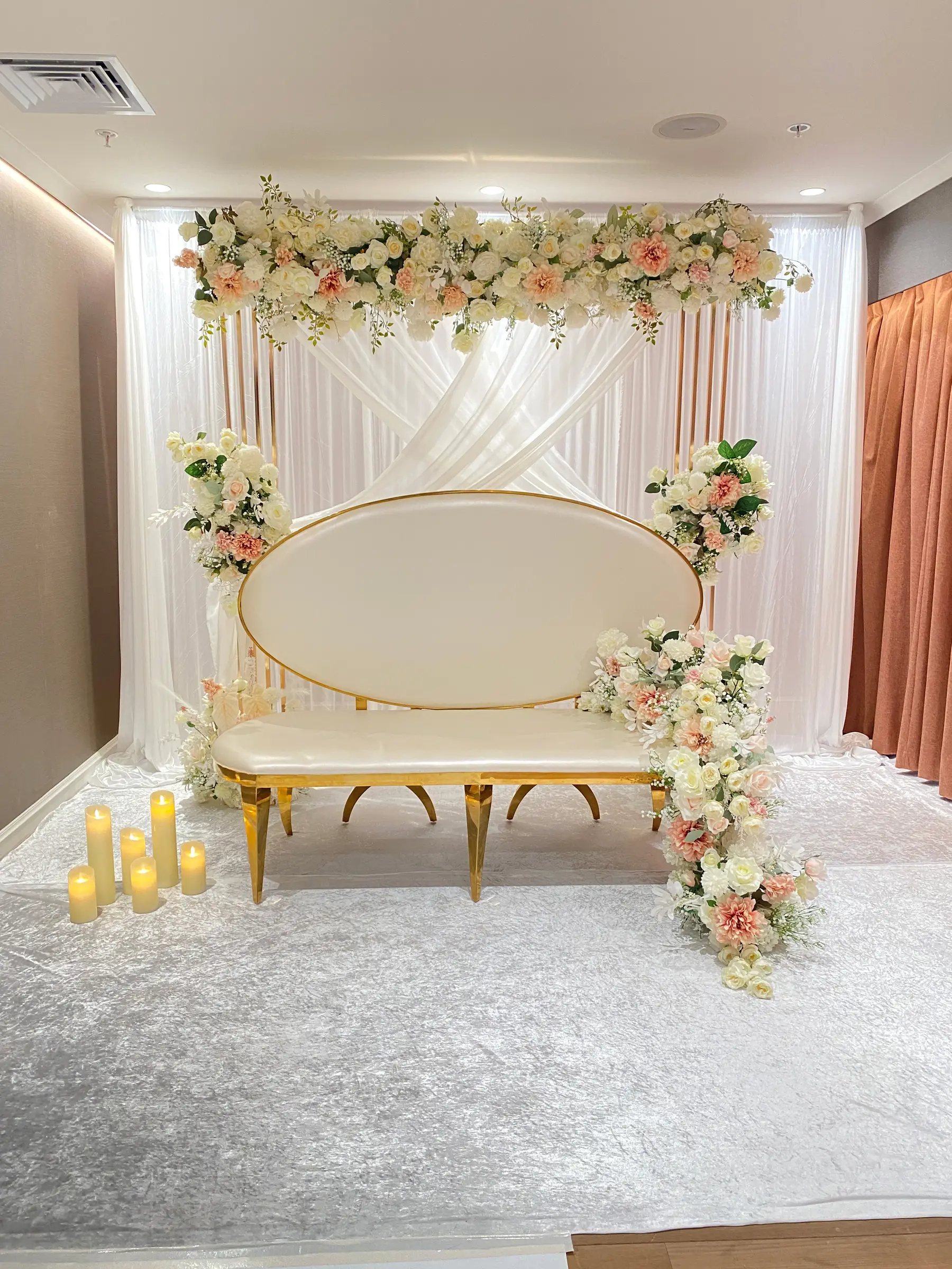 Stage styling by Decoration X: Gold oval-back sofa, crossed drapes, blush garland, LED candles.