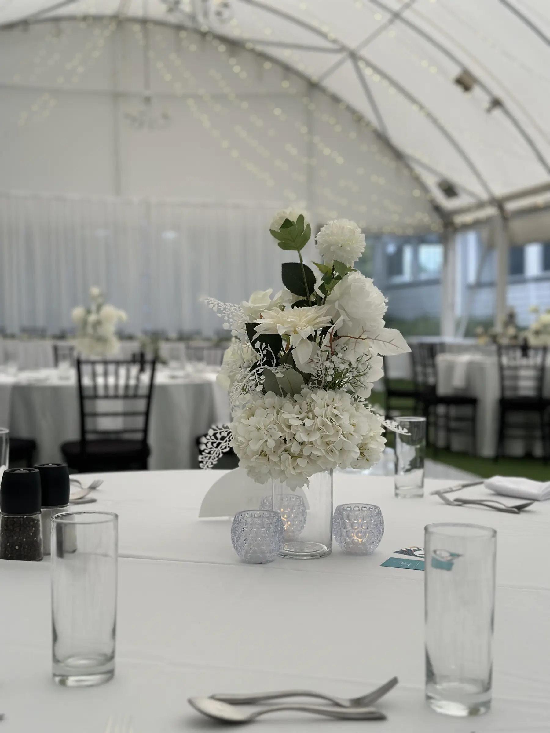 Tables styling by Decoration X: White floral centrepiece in marquee, chiavari chairs.