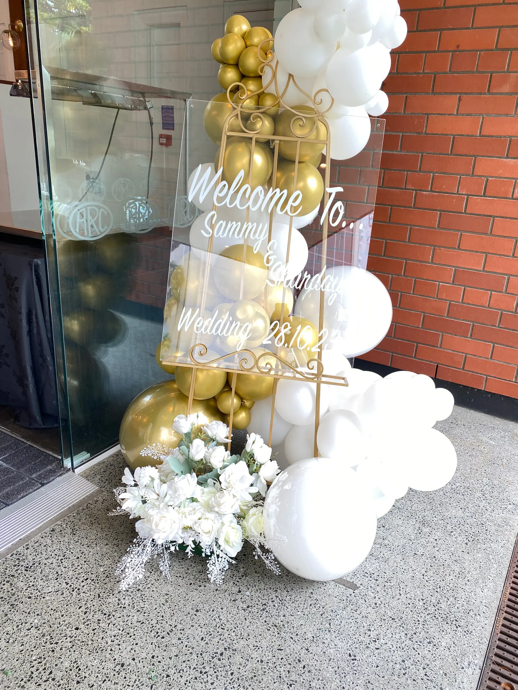 Signage styling by Decoration X: 'Welcome To Sammy & Sharday Wedding 28.10.23' acrylic sign, gold/white balloons.