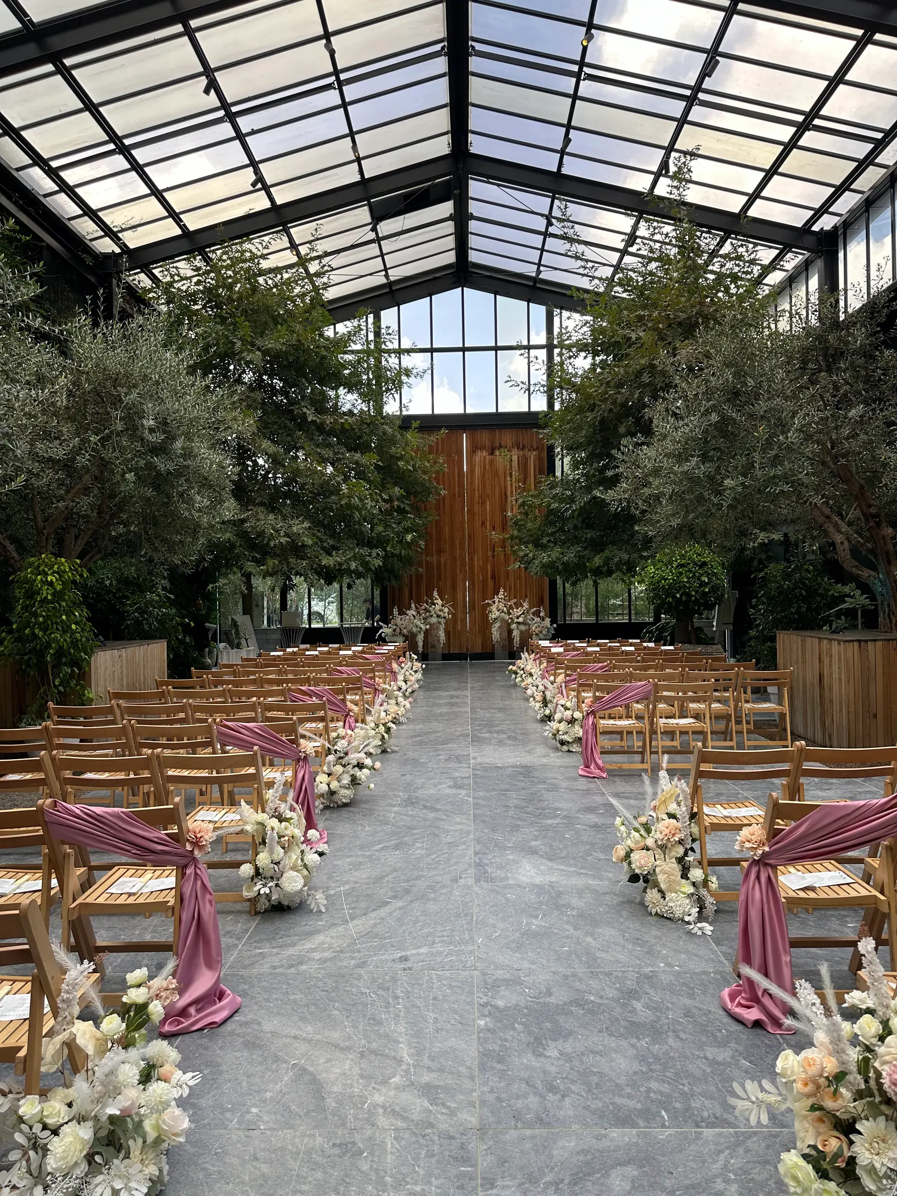 Ceremony styling by Decoration X: Glasshouse aisle, olive trees, rose chair sashes, timber doors.