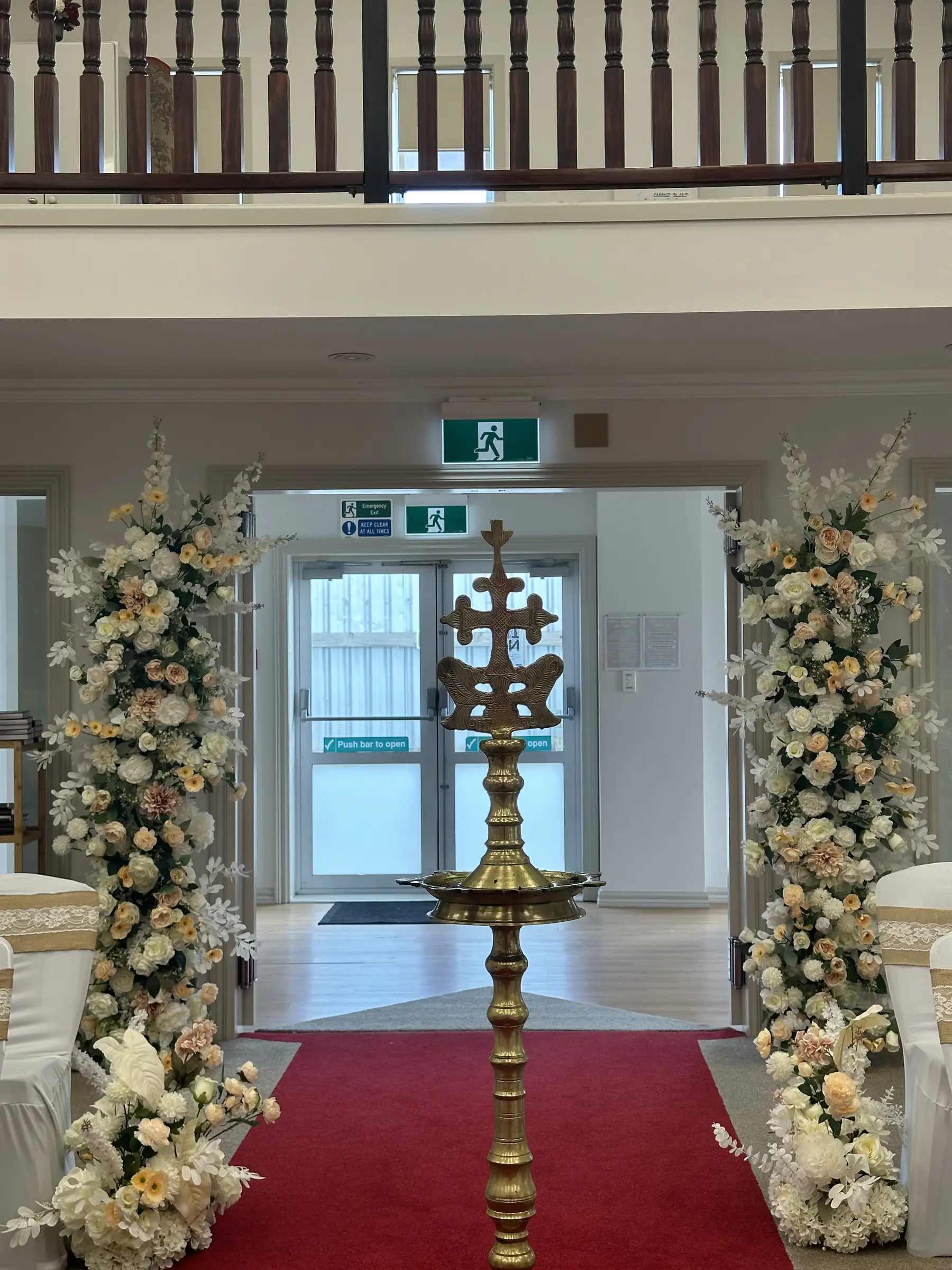 Ceremony styling by Decoration X: Church aisle, red carpet, gold cross stand, floral columns.