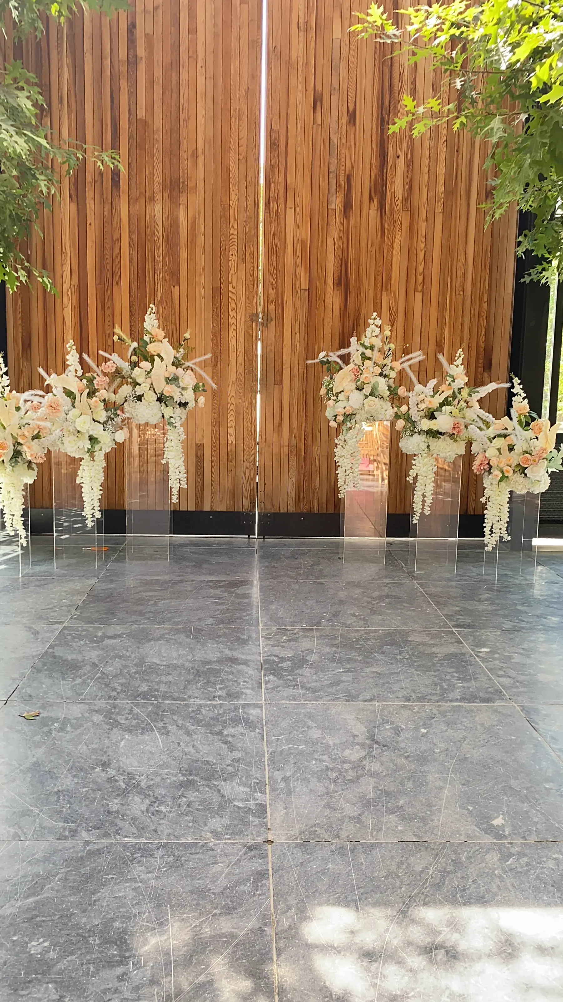 Ceremony styling by Decoration X: Acrylic plinths with white florals and pampas, timber wall, stone floor.