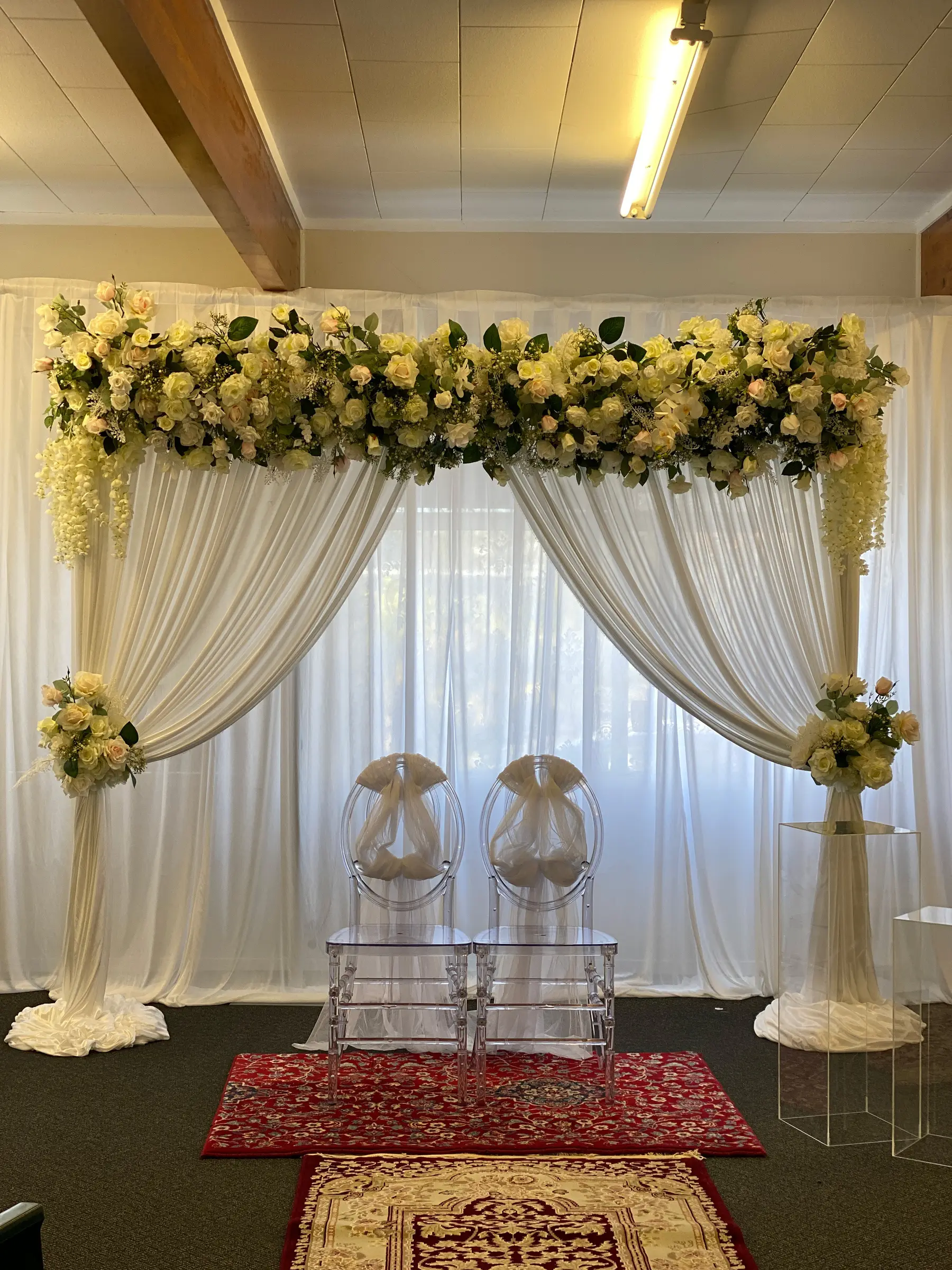 Ceremony styling by Decoration X: White/yellow floral arch, ghost chairs with tulle, red rug; fluorescent tube.