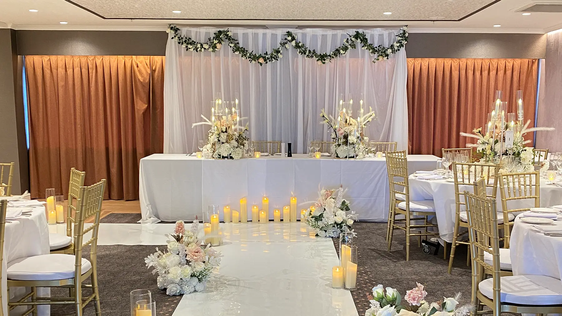 Reception styling by Decoration X: Hotel function room: bridal table, garland, gold chiavari, candle-lined aisle.