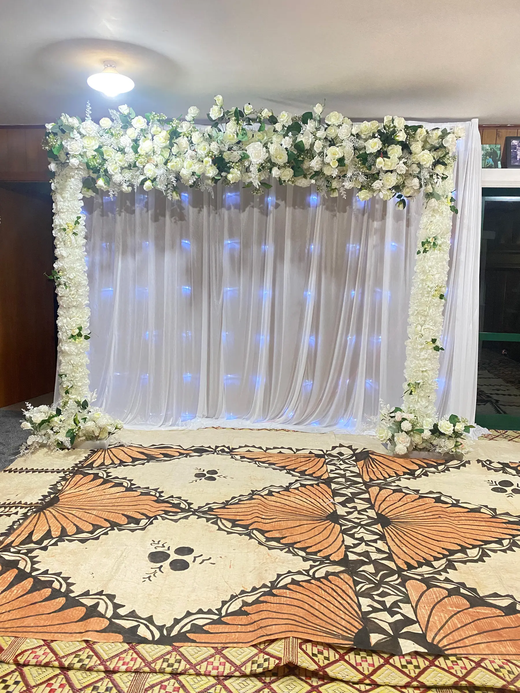 Reception styling by Decoration X: White drape backdrop with garland, Pacific-patterned hall floor.
