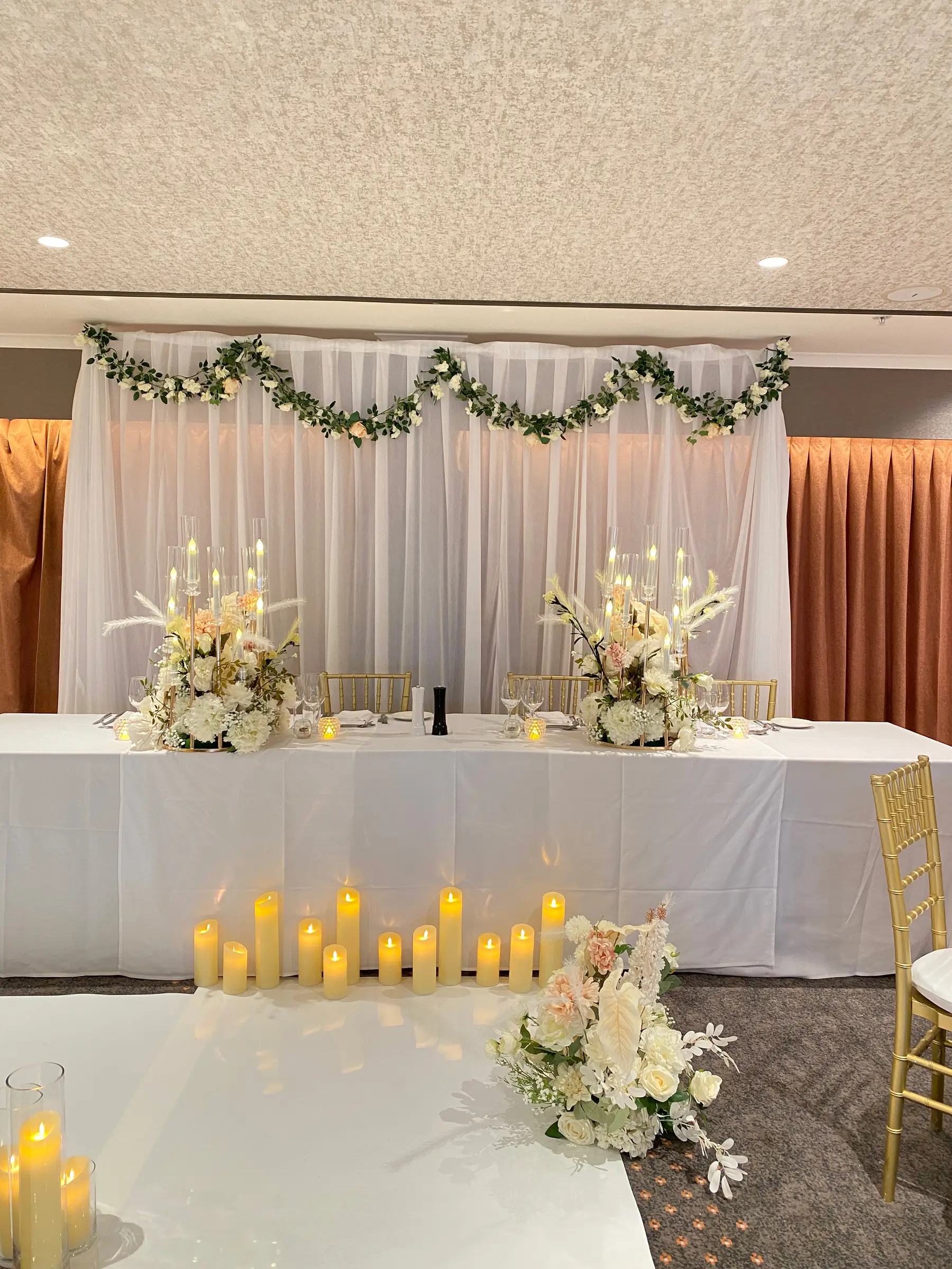 Reception styling by Decoration X: Bridal table, drape with garland, candle cluster, gold chiavari.